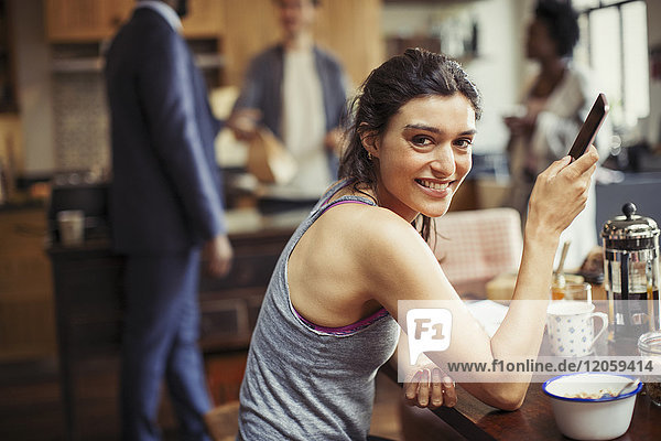 Portrait lächelnde junge Frau SMS mit Smartphone am Frühstückstisch