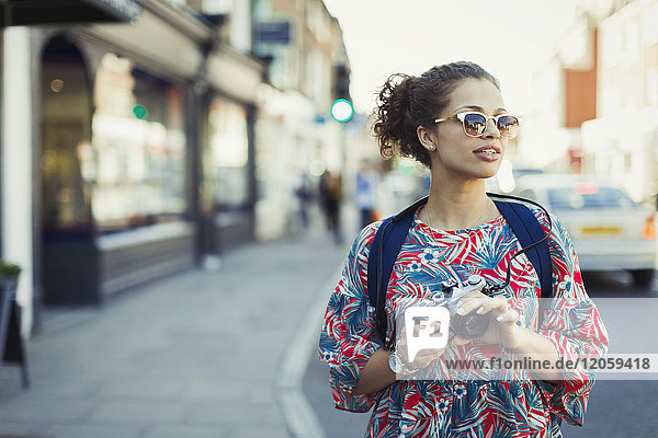 Young female tourist in sunglasses with camera on urban street