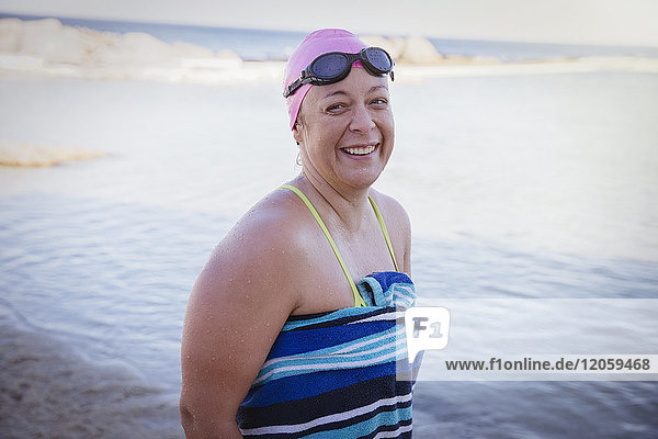 Porträt eines lächelnden Schwimmers in Handtuch gewickelt am Strand des Meeres