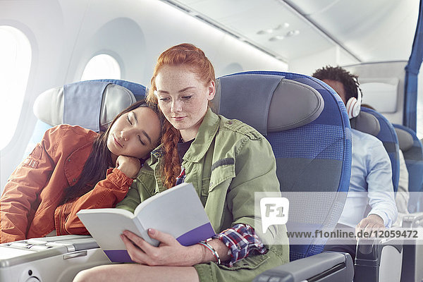 Liebevolles junges lesbisches Paar beim Schlafen und Lesen im Flugzeug