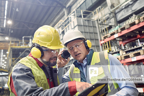 Stahlarbeiter tragen Gehörschutz mit digitaler Tablette im Stahlwerk