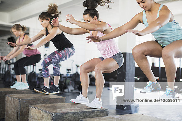 Determined women doing jump squats on boxes in exercise class