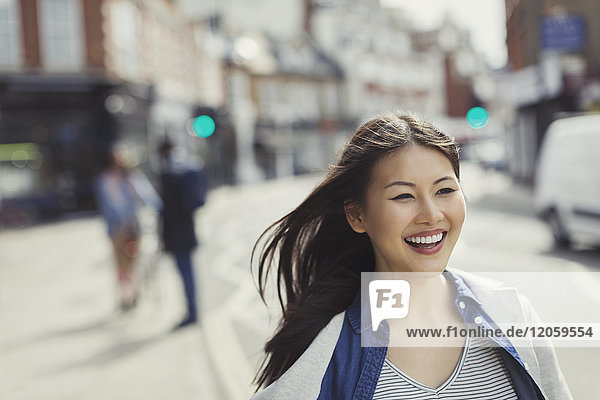Lächelnde  enthusiastische junge Frau  die auf einer sonnigen  städtischen Straße geht.