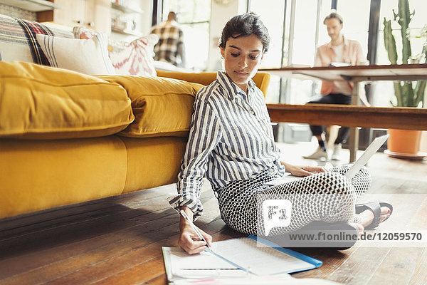 Female freelancer working at laptop  writing on paperwork in living room