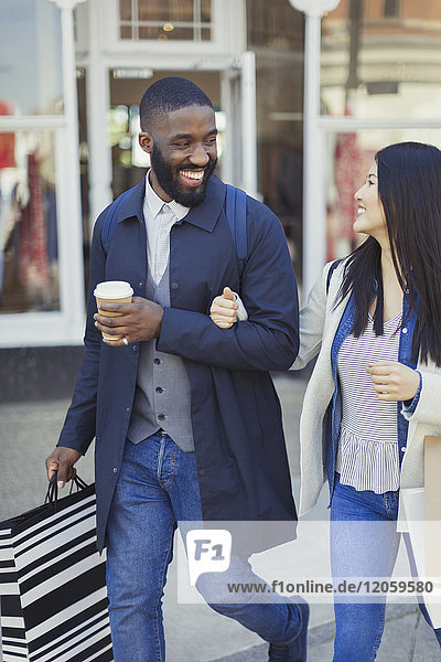 Smiling young couple walking along storefront with coffee and shopping bags