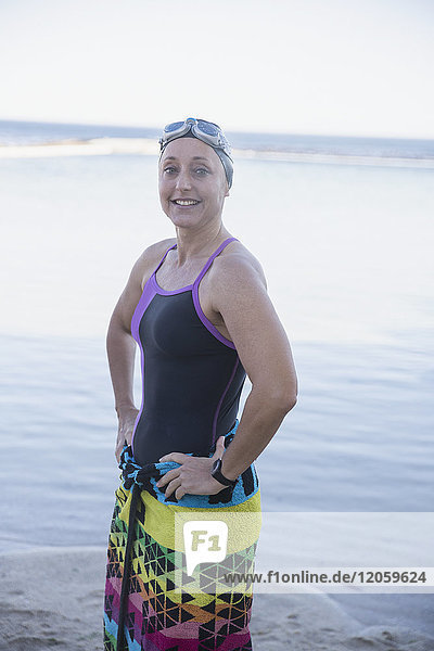 Portrait lächelnde  selbstbewusste Schwimmerin in Handtuch gewickelt am Meeresstrand