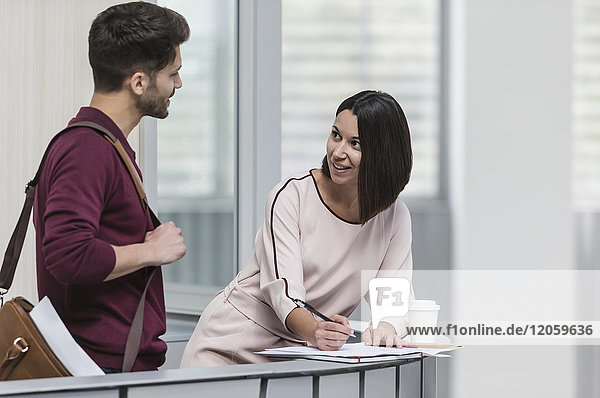 Businessman and businesswoman discussing paperwork at railing in office