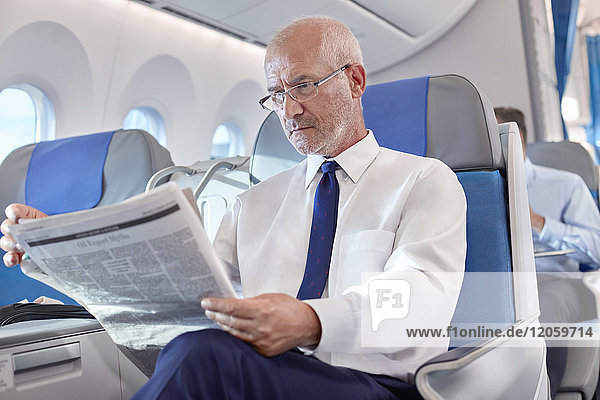 Senior Geschäftsmann beim Zeitungslesen im Flugzeug
