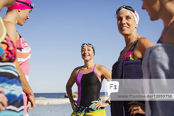 Smiling female open water swimmers wrapped din towels on sunny beach