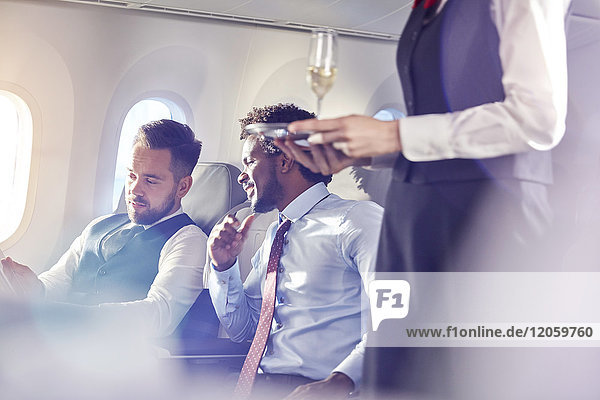 Flugbegleiter  der Geschäftsleuten in der ersten Klasse im Flugzeug Champagner serviert.
