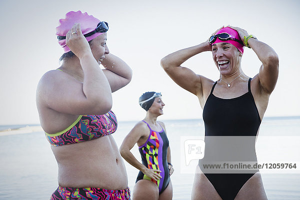 Lächelnde Schwimmerinnen beim Einstellen der Badekappen am Meer