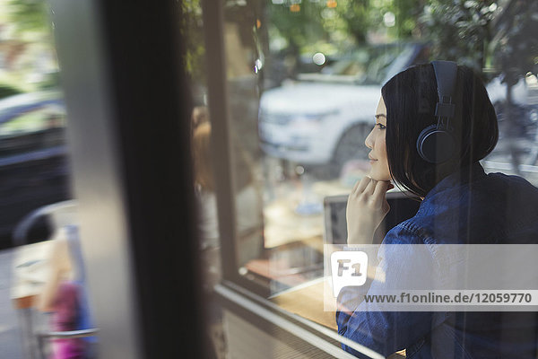 Nachdenkliche junge Frau hört Musik mit Kopfhörern und schaut weg zum Café-Fenster
