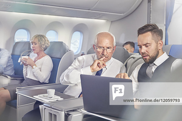 Geschäftsleute bei der Arbeit am Laptop in der ersten Klasse im Flugzeug