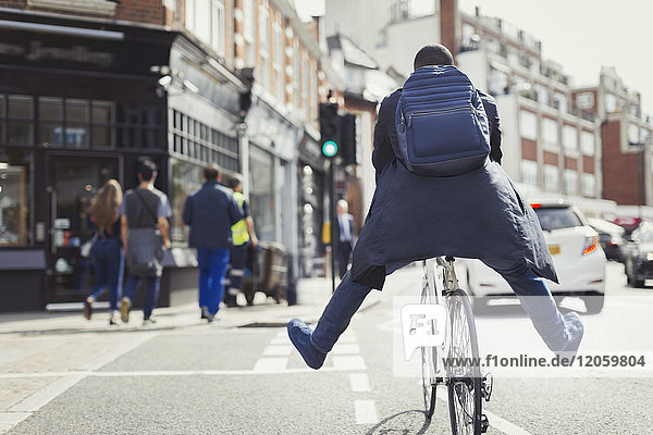 Verspielter junger Geschäftsmann beim Pendeln,  Fahrradfahren auf sonniger Stadtstraße