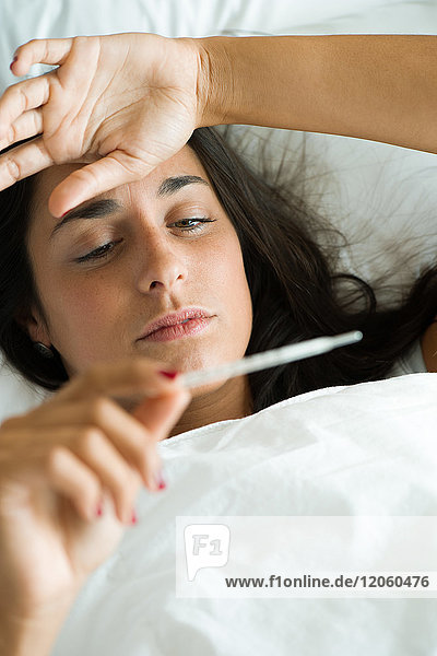 Woman lying in bed taking temperature with thermometer
