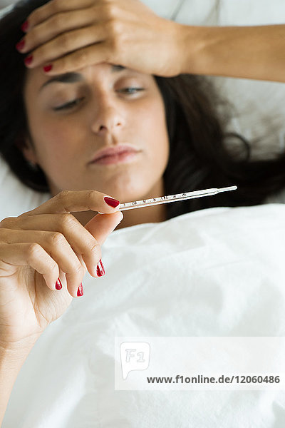 Frau im Bett liegend  Temperaturmessung mit Thermometer