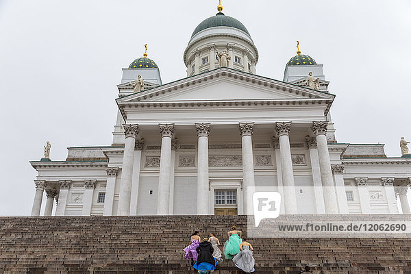 Gruppe von Frauen in farbenfrohen Kleidern  die die Stufen der lutherischen Kathedrale in Helsinki  Finnland  hinaufgehen.
