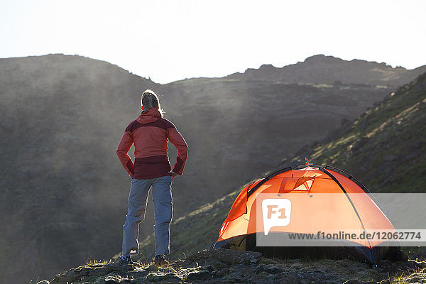 Rear view of woman standing in the mountains  next to a tent  sunrise.