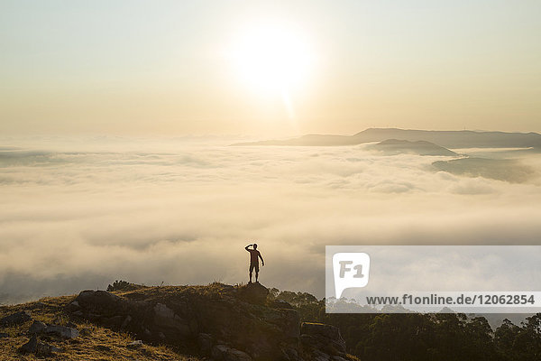 Rear view of man standing on top of mountain  admiring landscape view across misty valley.