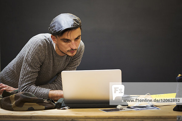 A man in a leather cap using a laptop computer.