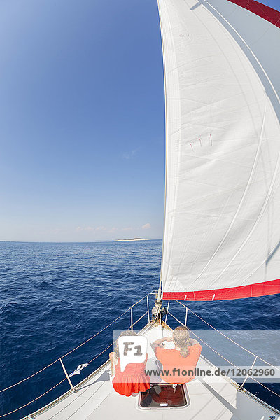 High angle rear view of man and woman sitting side by side near the bow on a sailing yacht on the Adriatic Sea.