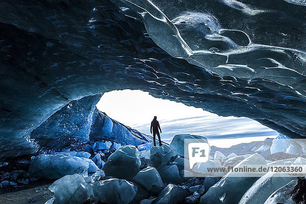 Rear view silhouette of person standing on ice rock at the entrance to a glacial ice cave.