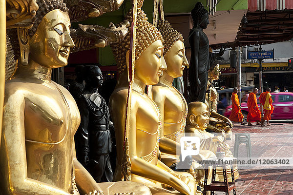 Tall golden Buddha statues lined up on a pavement.