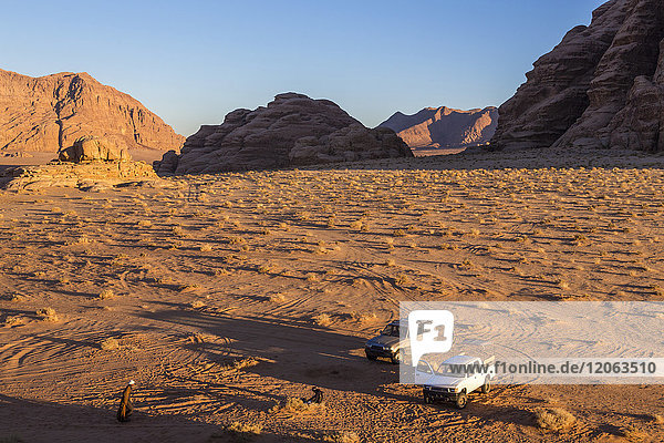Zwei Autos parken in einer Wüstenlandschaft mit Felsen und Bergen.
