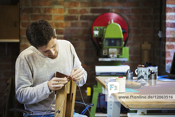 Ein Handwerker in einer Werkstatt  der Kordel oder Schnur durch ein kleines handgefertigtes Objekt fädelt.