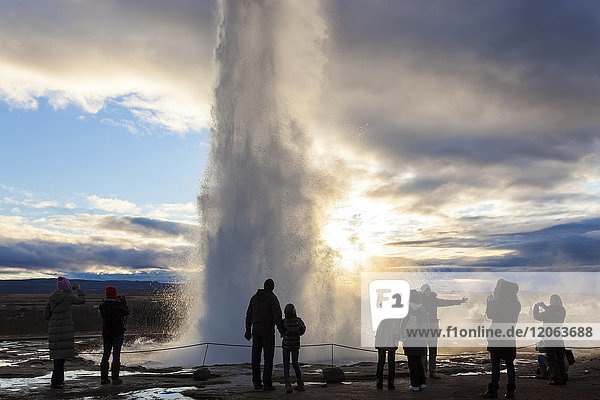 Silhouette of group of people standing around fountain of geyser at twilight.
