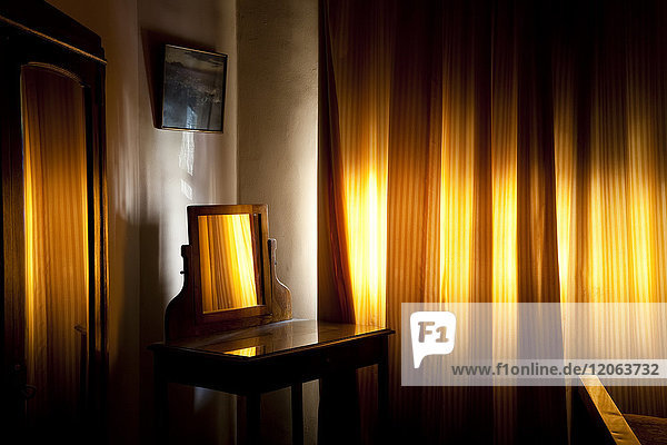 Room interior with vintage wooden dressing table with mirror  yellow light filtering through drawn curtains.