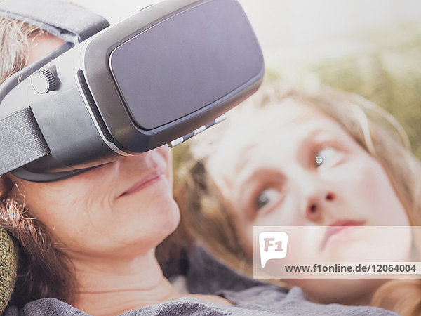 Mädchen betrachtet ihre Mutter mit einem Virtual-Reality-Headset  während sie sich auf dem Sofa entspannt