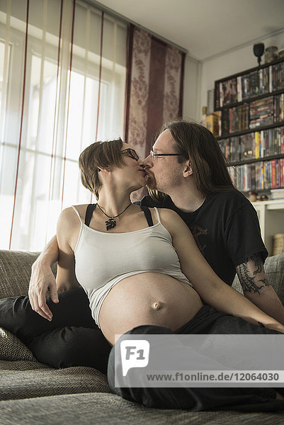 Ein schwangeres Paar küsst sich auf der Couch