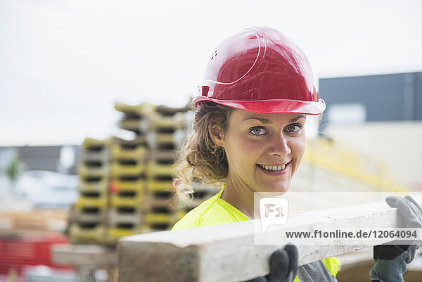 Weiblicher Bauarbeiter  der auf einer Baustelle eine Holzplanke trägt