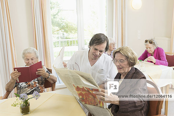 Pflegerin liest Zeitung mit älterer Frau im Altersheim