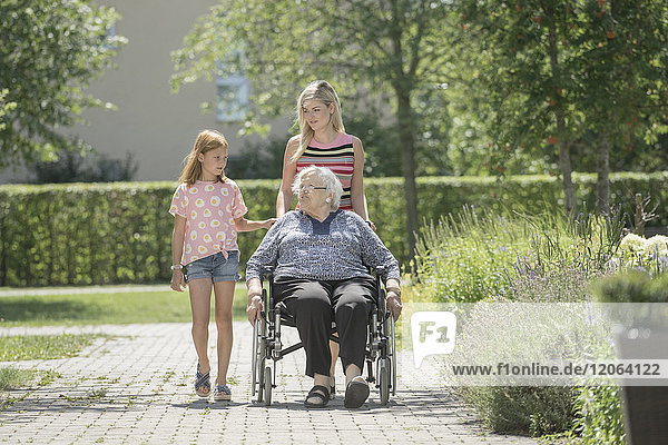 Ältere Frau im Rollstuhl mit Tochter und Enkelin im Altenheimpark