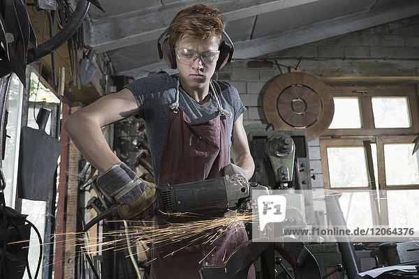 Auszubildender Schmied schneidet Eisenstange mit Winkelschleifer in der Werkstatt