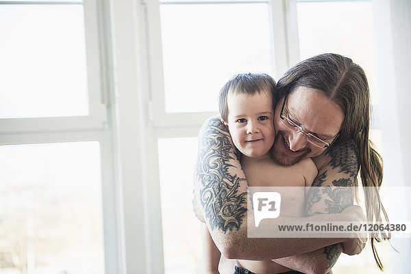 Tätowierter Vater  der seinen Sohn zu Hause umarmt