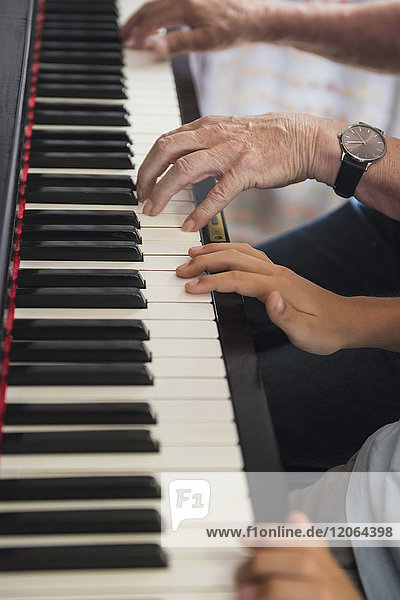 Hands of grandfather and grandson playing piano