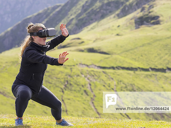 Frau übt Tai-Chi-Bewegungen mit Virtual-Reality-Brille auf einem Berg