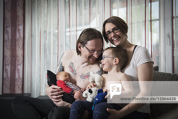 Porträt der Eltern mit neugeborenem Baby und kleinem Sohn auf dem Sofa sitzend