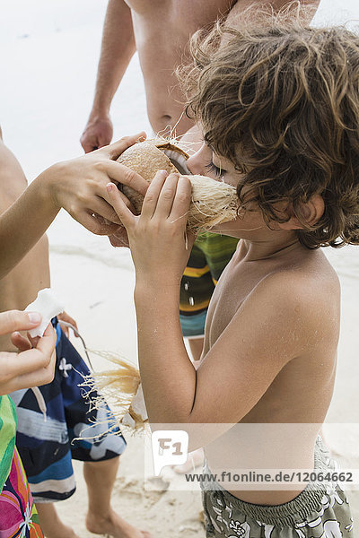 Kinder teilen sich eine Kokosnuss am Strand