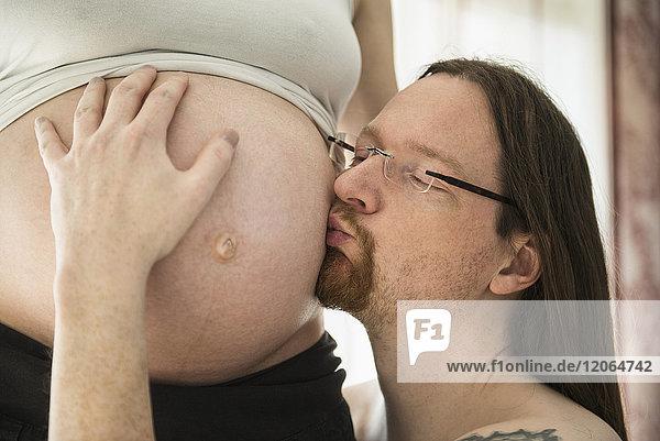 Mann küsst den Bauch seiner schwangeren Frau