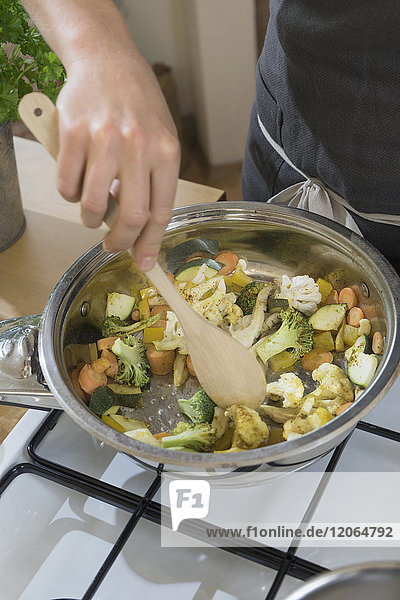 Woman stirring vegetables with spoon in pan