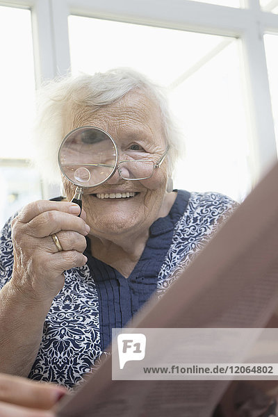 Senior woman reading newspaper with magnifier glass