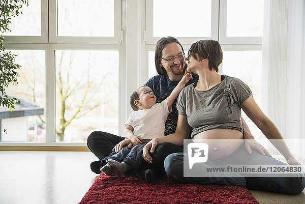 Schwangere Mutter mit Vater und Sohn auf dem Teppich sitzend