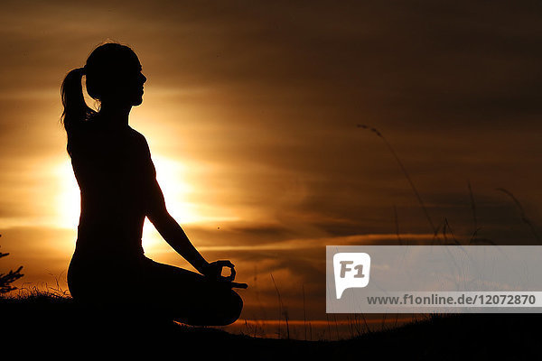 Silhouette of a woman practicing yoga against the light of the evening sun. Lotus position. French Alps. France.