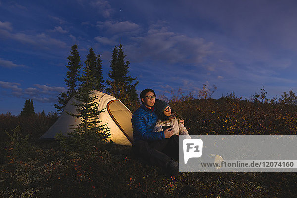 Couple sitting in front of an illuminated tent  Alaska  United States of America  North America