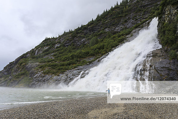 Visitor with outstretched arms on a beach in front of Nugget Falls Cascade  Mendenhall Lake and Glacier  Juneau  Alaska  United States of America  North America