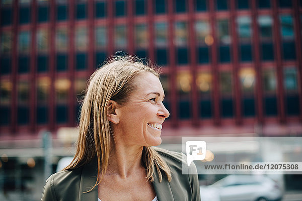 Smiling mature businesswoman looking away against building in city
